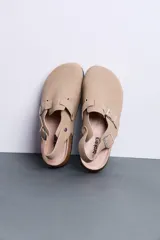Sandalias estilo zueco color beige con tira trasera ajustable, hebillas metálicas plateadas, suela de corcho y base de goma negra.