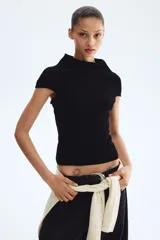 Top en punto suave, de color negro, corte ceñido al cuerpo, cuello alto y mangas cortas con aberturas en los hombros.