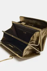 Bolso de hombro de formato rígido en piel metalizada color dorado. Presenta un diseño con pespuntes decorativos, triple compartimento interno y cierre principal mediante imán. Incluye doble asa de hombro en cadena metálica.