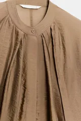 Camisa fluida de Zara Woman Collection, confeccionada en hilatura con mezcla de viscosa en tono tostado. Presenta cuello redondo, mangas largas con puños elásticos y diseño fruncido en la parte delantera. Dispone de cierre frontal con botones ocultos por solapa.