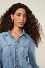 Camisa de jean celeste de corte clásico, con cuello, mangas largas, bolsillos frontales y cierre de botones.