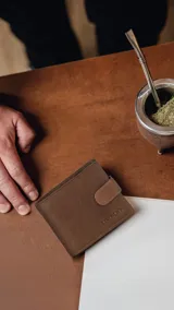 Billetera de hombre color marrón claro, tipo plegable, con cierre de presilla y broche. Presenta múltiples compartimentos internos para tarjetas y billetes, y un compartimento con cierre para monedas.