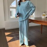 Conjunto de pijama de dos piezas confeccionado en tela de plush texturizada con diseño de rayas verticales en relieve. Incluye una remera de manga larga con cuello redondo y un pantalón de corte holgado. La remera presenta un pequeño bordado decorativo en el pecho.