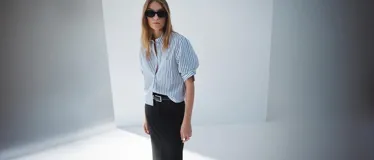 Camisa de corte recto y diseño crop, con estampado de rayas verticales en azul y blanco. Presenta cuello camisero, cierre frontal con botones y un bolsillo en el pecho.