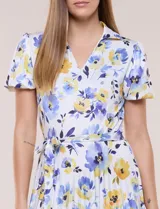 Vestido midi de seda fría blanca con estampado floral en tonos azules y amarillos, escote en V con cuello solapa, mangas cortas, lazo ajustable en la cintura y falda plisada.