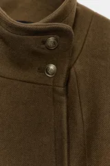 Chaqueta corta de paño color verde militar, con cuello subido, manga larga con puños abotonados y cierre frontal cruzado con botones metálicos. Presenta hombreras y bolsillos de vivo en el delantero.