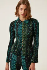 Camisa plisada negra con estampado floral en tonos verdes y azules, cuello camisero, botones dorados y mangas largas acampanadas.