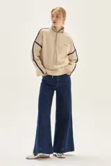 Sweater de tejido de punto color beige, con cuello redondo y detalles de bordado en zigzag en color azul oscuro a lo largo de las mangas y hombros. Presenta un pequeño bordado con texto en el pecho.