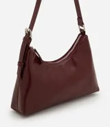 Cartera tipo baguette de tamaño pequeño en cuero sintético color bordó, con correa ajustable y cierre de cremallera metálica con herrajes en níquel.