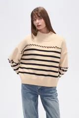 Sweater de punto color beige con rayas horizontales color crema, cuello alto y corte holgado. Presenta costuras decorativas en hombros y pecho.