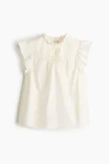 Top de algodón color beige claro con cuello de volados, canesú en V con jaretas y detalles bordados al frente, y mangas circulares con volados.