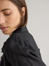 Camisa de lino color negro, con cuello clásico, cierre frontal de botones de madera y detalle de volados en los hombros. Presenta costuras a la vista en tono contrastante.