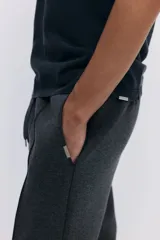 Pantalón tipo jogger de punto en tono gris oscuro, con cintura elástica y cordón ajustable. Presenta un pliegue cosido en el frente de cada pierna, bolsillos laterales y un bolsillo insertado trasero.