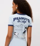 Remera de algodón color celeste con cuello y bordes de mangas en color azul marino. Presenta estampa frontal con el personaje Snoopy vestido con campera puffer y la inscripción Peanuts Ski Lodge.