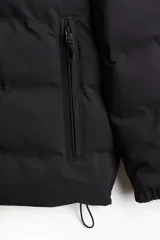 Campera puffer de diseño acolchado, con cuello elevado, capucha ajustable con cordón, cierre frontal, bolsillos laterales con cierre y puños elásticos.