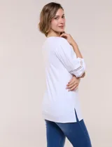 Remera blanca de silueta recta y algodón suave, con escote redondo y pequeña abertura central tipo gota. Presenta mangas de largo intermedio con aplicación horizontal de puntilla calada al tono y ruedo recto con tajos laterales.