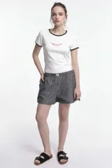 Remera baby blanca de algodón, de corte cropped al cuerpo y mangas cortas. Presenta ribetes negros en contraste en el cuello redondo y los puños, con un estampado localizado de un ají rojo con la inscripción 'Pimentón' en el centro del pecho.
