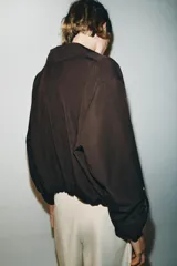 Blazer corto de color marrón oscuro, con cuello solapa, cierre frontal de botones y mangas largas con puños vueltos. Presenta un diseño con bajo elástico que le otorga una silueta ajustada en la cintura.