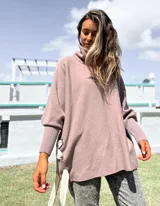 Polerón de punto color rosado viejo, con cuello alto, mangas anchas con puños acanalados y detalle de ojalillos metálicos con cintas en los laterales.