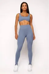 Conjunto deportivo de mujer color beige, compuesto por un top de tirantes anchos con escote curvado y calza de tiro alto con diseño sin costuras frontales.
