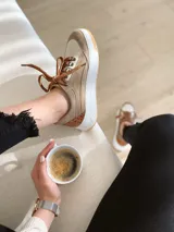 Championes de cuero color visón con cordones marrones, suela blanca y base color caramelo.