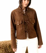 Chaqueta de gamuza marrón con cierre frontal mediante lazos de cuero y bolsillos frontales con solapa y botones metálicos.