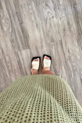 Vestido sin mangas, color verde oliva, tejido a crochet con patrón de rombos o calado abierto. Tiene cuello redondo y corte recto que cae hasta medio muslo.