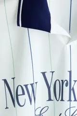 Camiseta de fútbol de manga larga H&M en malla estampada, color blanco con rayas verticales y cuello y puños en azul marino. Cuenta con diseño holgado y estampado frontal "New York League East Coast".