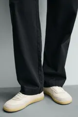 Zapatilla deportiva tipo barefoot confeccionada en piel color blanco roto con apliques de gamuza en tonos grises. Posee puntera redondeada y ancha, cierre mediante cordones al tono y suela de goma flexible en color caramelo con tecnología drop 0.