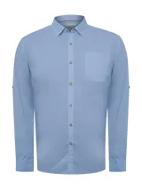 Camisa celeste de manga larga RKF Galiton, confeccionada en popelina 100% algodón orgánico. Cuenta con botones de madera, mangas ajustables, bolsillo de pecho con logo bordado y protección UPF +20.