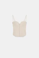 Top estilo corset de color beige, con escote corazón, tirantes finos ajustables y cierre frontal con ganchos metálicos.