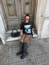 Bota de caña alta estilo biker, confeccionada en cuero sintético negro. Presenta una suela track con plataforma, puntera redondeada y un detalle de arnés con hebilla metálica y tachas en la zona del tobillo.