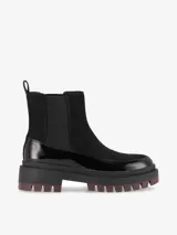 Botas Chelsea de caña baja color negro, combinadas en eco cuero charol y gamuza, con paneles elásticos laterales y suela track gruesa de goma con base dentada.