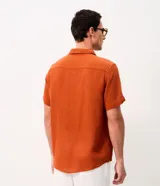 Camisa de manga corta color mostaza, confeccionada en algodón con textura, cuello inglés y cierre frontal de botones.