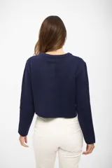 Saco de punto azul marino con cuello redondo, cierre frontal de botones y dos bolsillos delanteros tipo parche. Presenta mangas largas con puños acanalados y un diseño corto y estructurado.