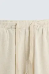 Pantalón de corte relajado color beige confeccionado en tejido de mezcla de algodón y lino. Posee cintura elástica ajustable con cordón, bolsillos frontales y bolsillos traseros de vivo.