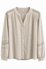 Blusa de manga larga color beige con escote en V y cuello mao. Presenta detalles de encaje y alforzas en los hombros y en las mangas.