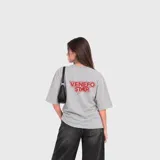 Remera gris melange de manga corta y corte oversize, con estampa en la espalda con la leyenda "VENEFO STAR" en color rojo.