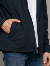 Campera rompeviento Calvin Klein de color azul marino, con cierre frontal de cremallera, capucha ajustable y bolsillos laterales. Presenta un parche con el logo de la marca en la manga y puños elásticos.