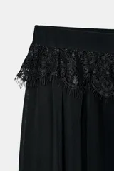 Pantalón bombacho negro, de tiro medio y cintura elástica, con detalle de encaje a tono en la cintura y bajo acabado en volante.