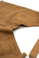 Bolso de gamuza marrón, estilo hobo, con correa para el hombro y detalles de argollas metálicas.