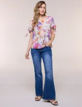 Blusa de gasa liviana con estampado floral en tonos violeta y rosado, cuello redondo y mangas cortas con detalle de lazo en los puños.