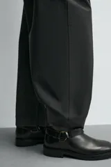 Bota de caña media fabricada en piel color negro, con detalle de arnés y hebilla metálica lateral. Presenta horma cuadrada y suela a tono con ligero tacón.