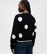 Suéter de punto con estampado de lunares blancos sobre fondo negro, cuello redondo, sisa desplazada y corte ligeramente corto.