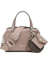 Cartera tipo satchel de Calvin Klein en color rosado con textura granulada. Cuenta con asa superior, correa ajustable extraíble y un set de accesorios colgantes que incluye un monedero circular con monograma y un pequeño estuche tipo sobre.