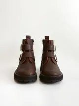 Botas cortas de cuero color marrón con suela track negra. Presentan dos correas ajustables con hebillas metálicas plateadas en el empeine y cierre lateral interno.