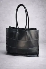 Bolso tote grande de cuero natural en color marrón, con diseño de piezas unidas mediante costuras visibles y asas de hombro.