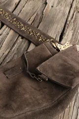 Bandolera confeccionada en cuero de gamuza marrón, con cierre superior. Presenta un llavero colgante con forma de estrella revestido en tachas metálicas y tiras flecadas en tono dorado.