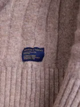 Sweater de punto en color beige, con cuello alto y cierre frontal parcial de botones. Presenta mangas largas con puños acanalados y diseño de corte clásico.