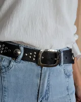 Cinturón de cuero marrón oscuro con tachas metálicas redondas en tonos bronce, plata y dorado. Hebilla rectangular de metal con acabado envejecido.